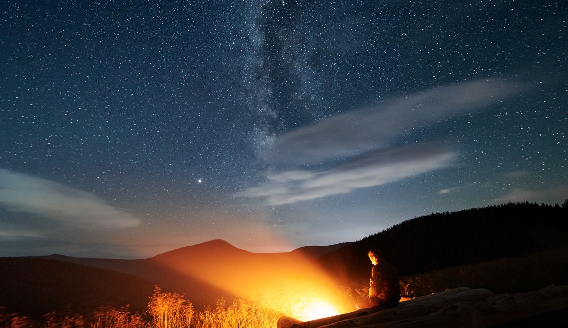 Silhouette of man resting in mountains near bonfire.